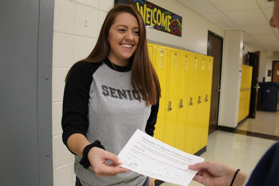 With a big smile on her face, Jessica Klimpel (12) hands a student a T-shirt order form on Oct. 11.