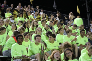 The band sits in the stands during a football game.