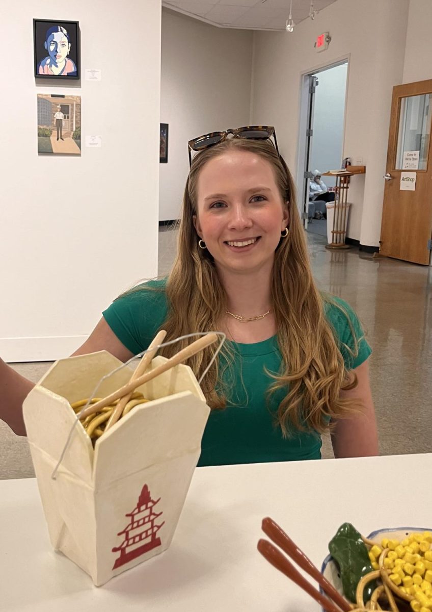 Baker happily poses with her displayed project in the St. Louis Artists Guild. I really enjoyed making the noodles using the clay extruder, Baker said. The extruder is her favorite tool to use in ceramics class. 